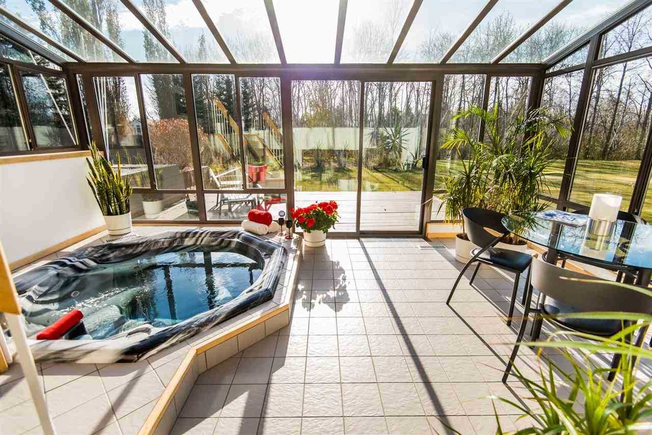 Sunroom with black-framed windows, light tiles, plants and a hot tub