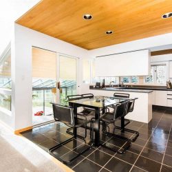 White-walled kitchen with wood ceiling and black tile floor; black dining table and chairs; white island and cabinets