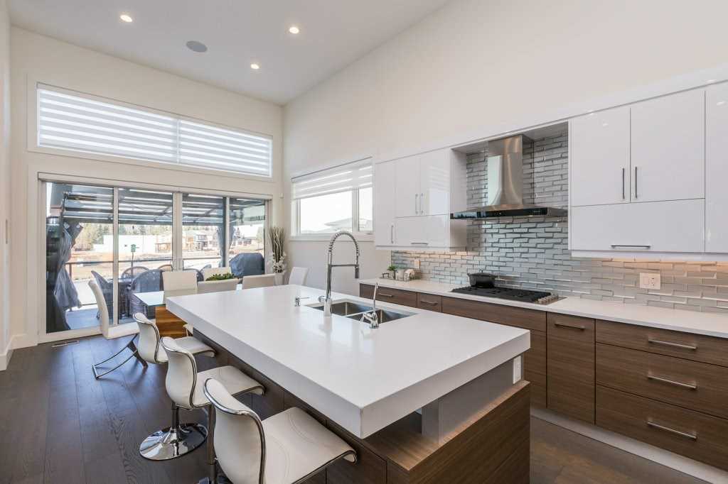 Kitchen with hardwood floor and white counters, upper cabinets and walls, wood cabinets below; tiered island with white counter and wood bottom, three white chairs and a sink