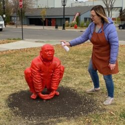 A woman spray painting a statue of a man squatting down