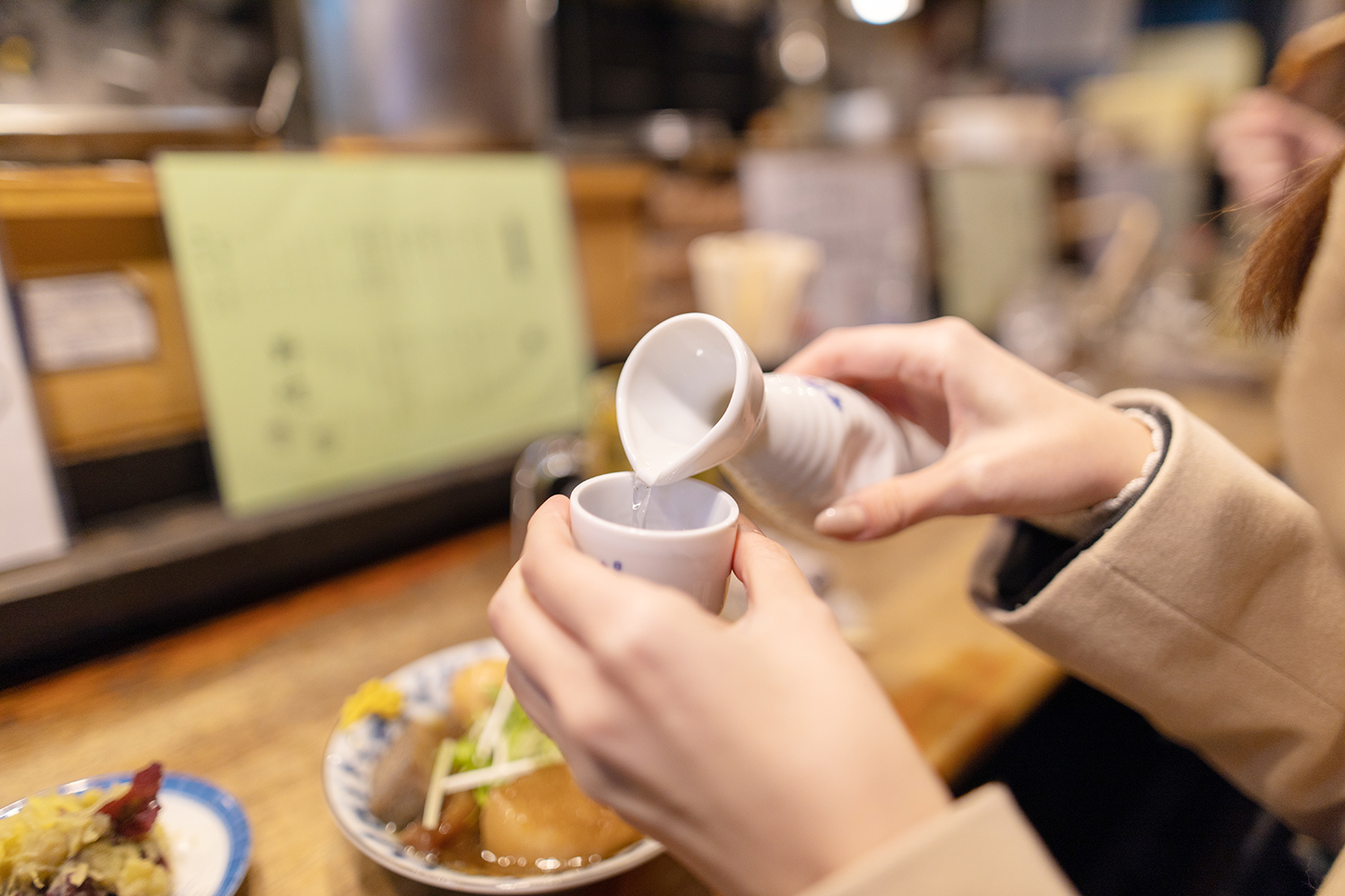 Young woman drinking Japanese Saki at Izakaya bar counter